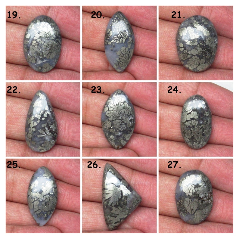 May include: Nine cabochon cut, polished, gray and silver pyrite stones with a variety of shapes, including oval, teardrop, and triangular. The stones are arranged in three rows of three.