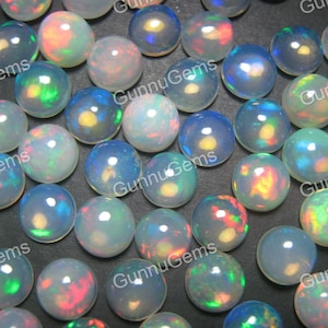 Op de afbeelding: Een verzameling ronde, iriserende opaal cabochons in verschillende tinten wit, blauw, groen en roze. De cabochons zijn glad en gepolijst, met een hoogglans afwerking.