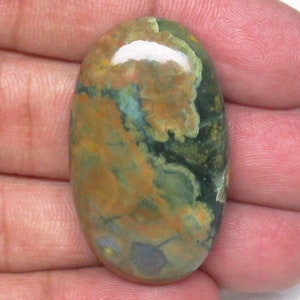 May include: A green, brown, and orange oval-shaped gemstone with a mottled pattern.