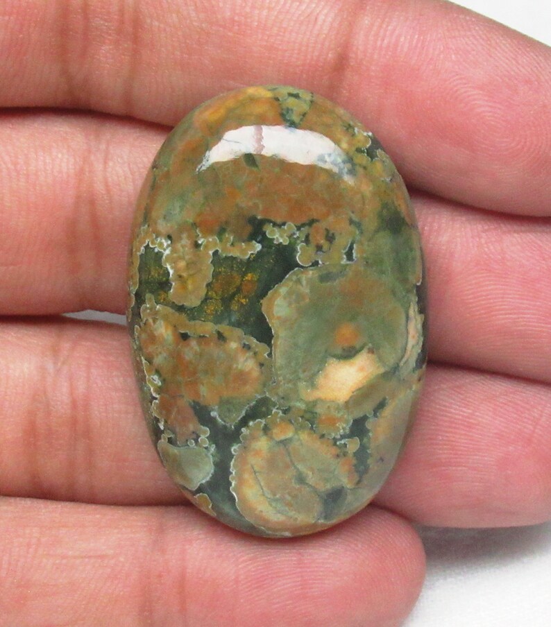 May include: A green, brown, and white oval-shaped cabochon gemstone with a mottled pattern.