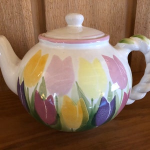 May include: White ceramic teapot with a rope-like handle and a floral design of pink, yellow, and purple tulips.
