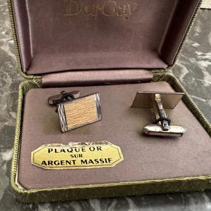 Op de afbeelding: Vintage gouden en zilveren manchetknopen in een bruine etui. De manchetknopen hebben een rechthoekig ontwerp met een getextureerd goudkleurig midden en zilveren randen. De etui is gevoerd met bruine stof en heeft een gouden label met de tekst "PLAQUE OR SUR ARGENT MASSIF".