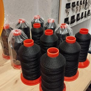 Op de afbeelding: Close-up van tien spoelen zwarte draad met rode plastic doppen. De spoelen zijn in een rij op een houten oppervlak gerangschikt.