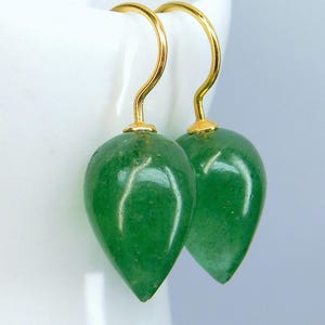 May include: A pair of green aventurine gemstone earrings. Each earring features a teardrop-shaped green stone suspended from a gold-colored hook. The earrings are displayed against a white background.