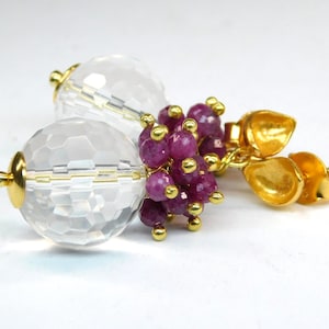 Könnte beinhalten: Goldene Ohrringe mit einer klaren Kristallperle und einem Cluster aus rosafarbenen Rubinperlen.