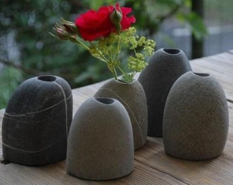 Könnte beinhalten: Fünf graue Steinvasen, jede mit einer anderen Form und Textur. Eine Vase enthält eine einzelne rote Rose und grünes Laub.