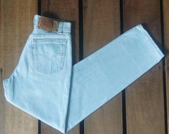 May include: Light blue denim jeans folded on a wooden surface. The jeans have a brown leather patch on the back waistband with the Levi's logo.