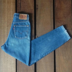 Puede incluir: Un par de pantalones vaqueros azules con un parche de cuero marrón que dice "Levi's" en la parte posterior. Los pantalones vaqueros están colocados sobre una superficie de madera.