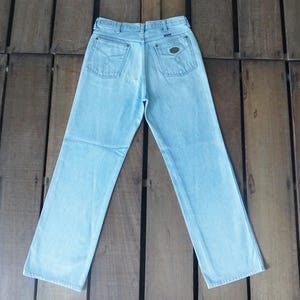 May include: Light blue denim jeans with a classic five-pocket design. The jeans have a straight leg cut and a faded wash. The back pockets feature a simple design, and there is a small patch on the back waistband.