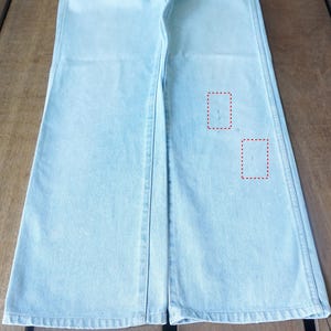 May include: Light blue denim pants with a wide leg design. The pants have a classic five-pocket style and a button and zipper closure. The denim has a faded wash and a slight distressed look.