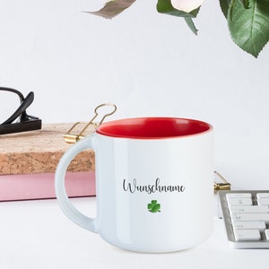 May include: White ceramic mug with a red interior and a black inscription that reads "Wunschname" with a green four-leaf clover.