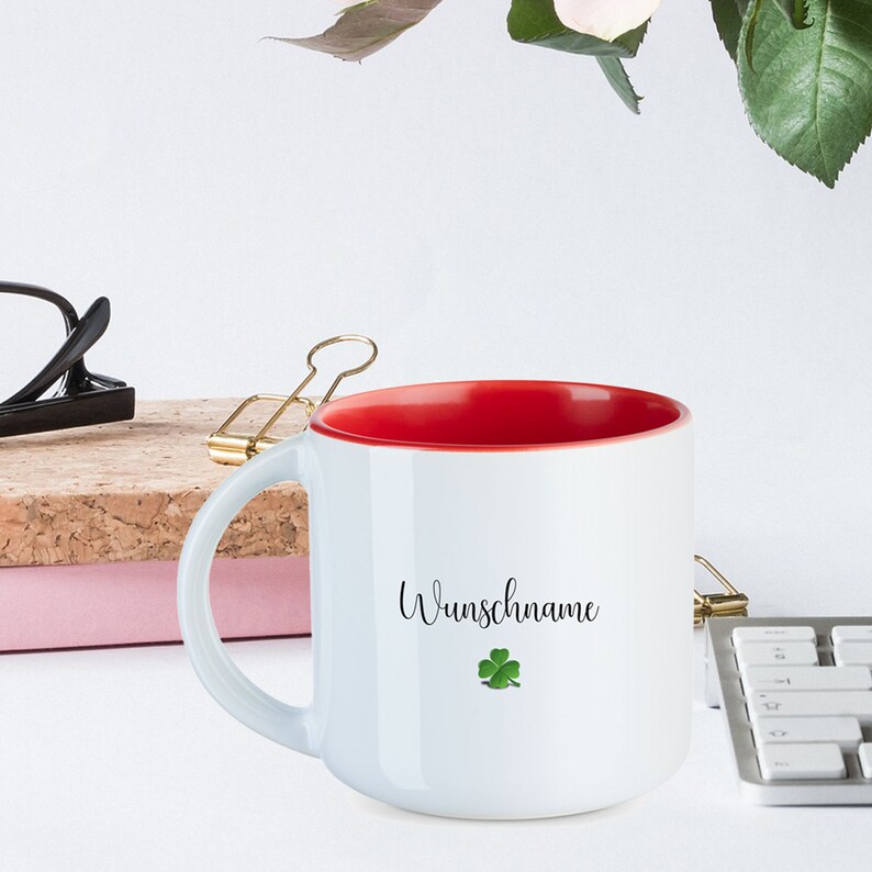 May include: White ceramic mug with a red interior and a black inscription that reads "Wunschname" with a green four-leaf clover.