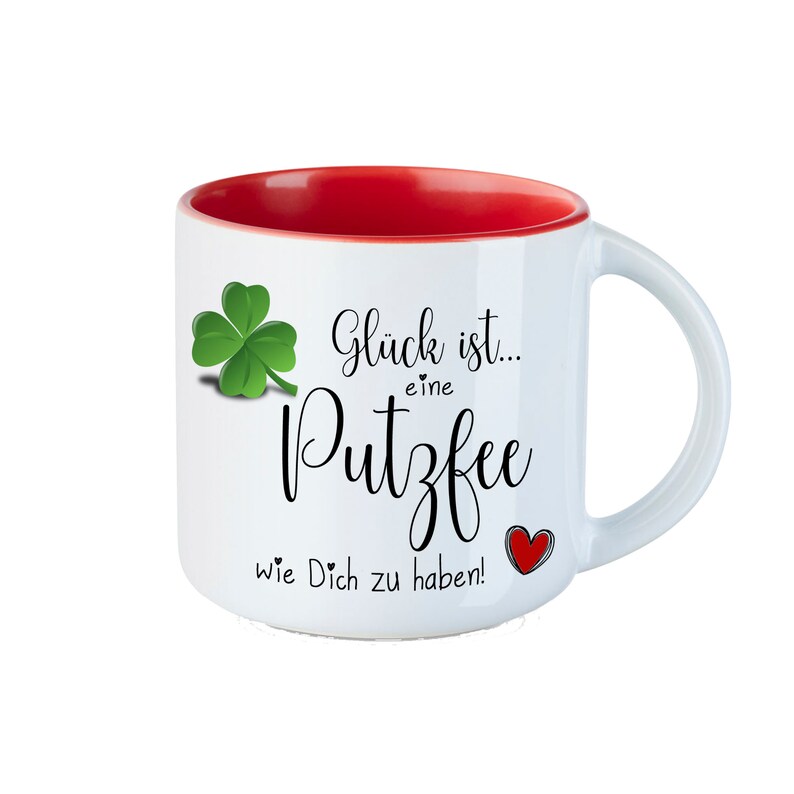 May include: White ceramic mug with a red interior. The mug has a green four-leaf clover and black text that reads "Gl&uuml;ck ist... eine Putzfee wie Dich zu haben!" with a red heart.