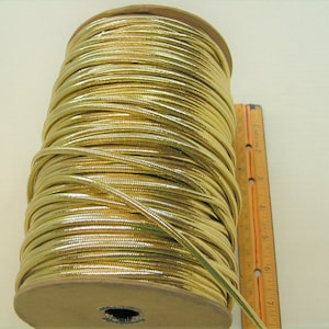 May include: A spool of gold metallic cord, approximately 18 cm long, with a ruler for scale.