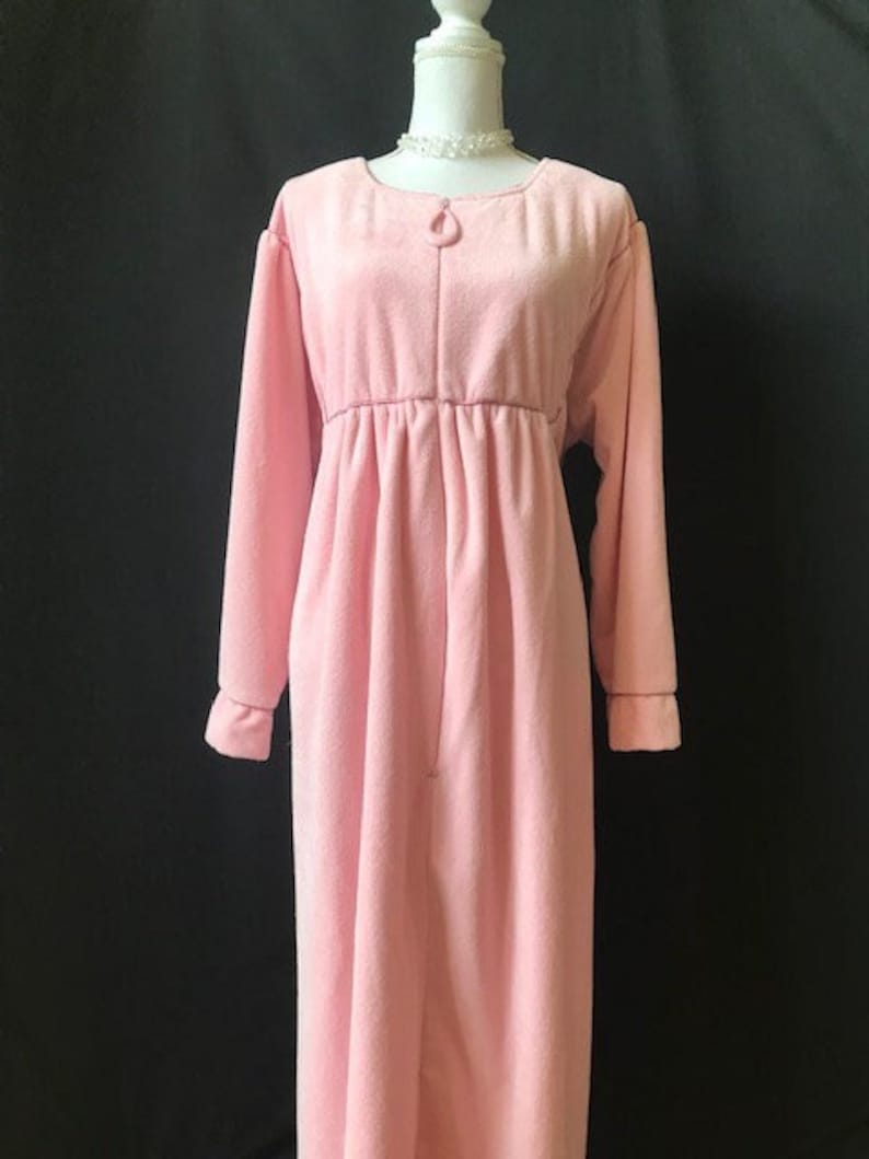 May include: A pink fleece robe with long sleeves and a zipper closure. The robe has a gathered waist and a simple design.