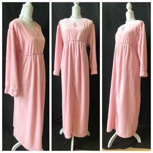 May include: A long, pink, velour robe with a tie at the neck and long sleeves. The robe has a gathered waist and a relaxed fit.