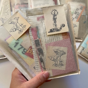 Peut inclure: Plusieurs petites pochettes transparentes remplies d'éphémères vintage. Chaque pochette contient des morceaux de papier, dont des pages de livres, du papier à motifs et des étiquettes numérotées. Certaines pochettes présentent des illustrations estampées de champignons et de bougies.