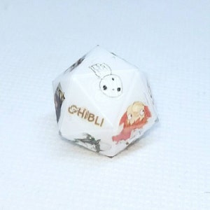 May include: A white, multi-sided die featuring illustrations of characters from Studio Ghibli films. The word "GHIBLI" is printed in gold. The die has various colorful images of animated characters.
