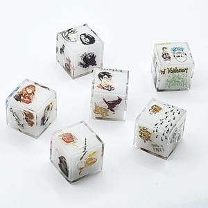 May include: Six clear acrylic cubes featuring various colorful illustrations and text related to the Harry Potter series. Each cube displays distinct character portraits, magical objects, and phrases like Lord Voldemort and Dobby is FREE.
