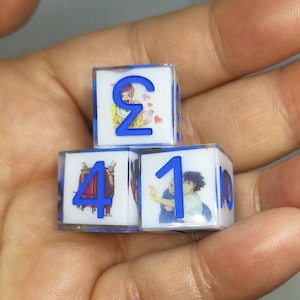 May include: Three clear plastic dice with blue numbers and colorful cartoon images. The dice show the numbers 2, 4, and 1.