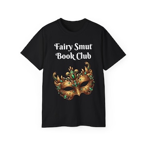 May include: Black t-shirt with the text "Fairy Smut Book Club" in white. Below the text is a gold and green mask design. The mask has intricate details and is adorned with green gemstones. The t-shirt is a casual wear item.
