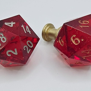 May include: Two red, clear, glittery, 20-sided dice with gold and silver numbers. The dice are attached to metal and brass knobs.