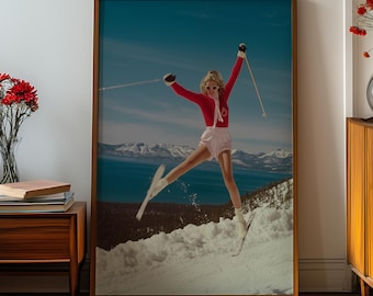May include: A framed print featuring a skier in a red ski suit and white shorts, mid-air on a snowy slope. The background shows a blue sky, mountains, and a lake. The print is in a wooden frame, adding a vintage aesthetic.