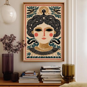 May include: A framed art print featuring a stylized illustration of Medusa. The artwork showcases a woman with black snake hair, red cheeks, and a gold collar. The background includes floral and sun motifs, with a pink and green border.
