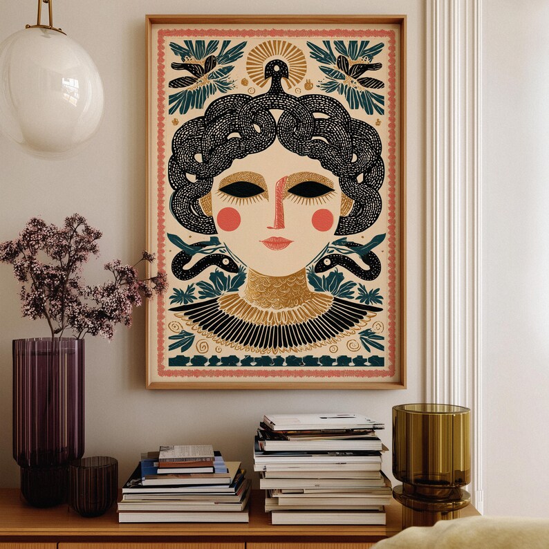 May include: A framed art print featuring a stylized illustration of Medusa. The artwork showcases a woman with black snake hair, red cheeks, and a gold collar. The background includes floral and sun motifs, with a pink and green border.