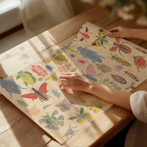 May include: A vintage-style wrapping paper featuring a colorful pattern of butterflies, beetles, and other insects. The paper is folded in half and a hand is reaching out to touch it.