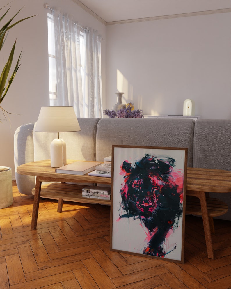 May include: A framed abstract painting of a lion with pink, black, and white paint. The painting is hanging on a wall in a living room with a wooden coffee table and a gray sofa.