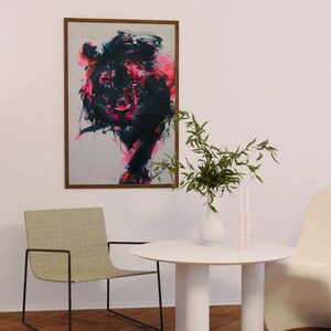 May include: A white round table with four white cylindrical legs. A vase with green leafy branches and a pink candle holder are on the table. A light brown woven chair with a black metal frame is in the foreground. A framed abstract painting of a pink and black animal is on the wall.