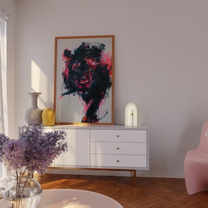 May include: A white dresser with three drawers and gold knobs. A lamp with a white base and a gold arch sits on top of the dresser. A framed painting of a colorful abstract animal hangs on the wall above the dresser. A pink chair sits in the corner of the room.