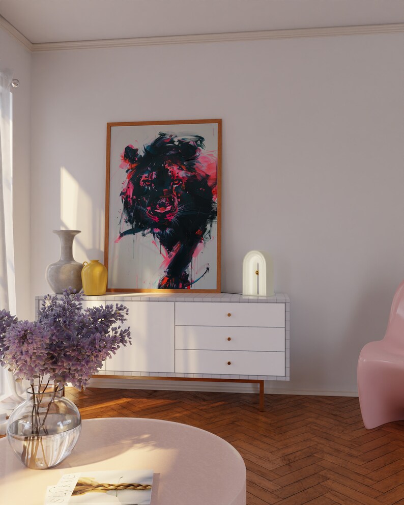 May include: A white dresser with three drawers and gold knobs. A lamp with a white base and a gold arch sits on top of the dresser. A framed painting of a colorful abstract animal hangs on the wall above the dresser. A pink chair sits in the corner of the room.