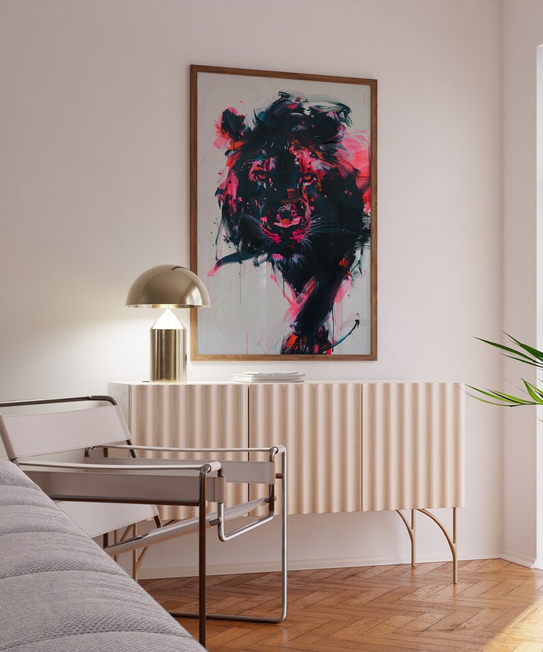 May include: A white chair with a metal frame sits in front of a light pink cabinet with gold legs. A gold lamp with a white shade sits on top of the cabinet. A framed painting of a black and pink lion hangs on the wall above the cabinet.