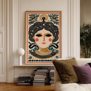 May include: A framed art print featuring a stylized illustration of a woman with black hair styled with snakes. The artwork has a beige background with a pink border and includes floral and snake motifs. The woman has red cheeks and lips.