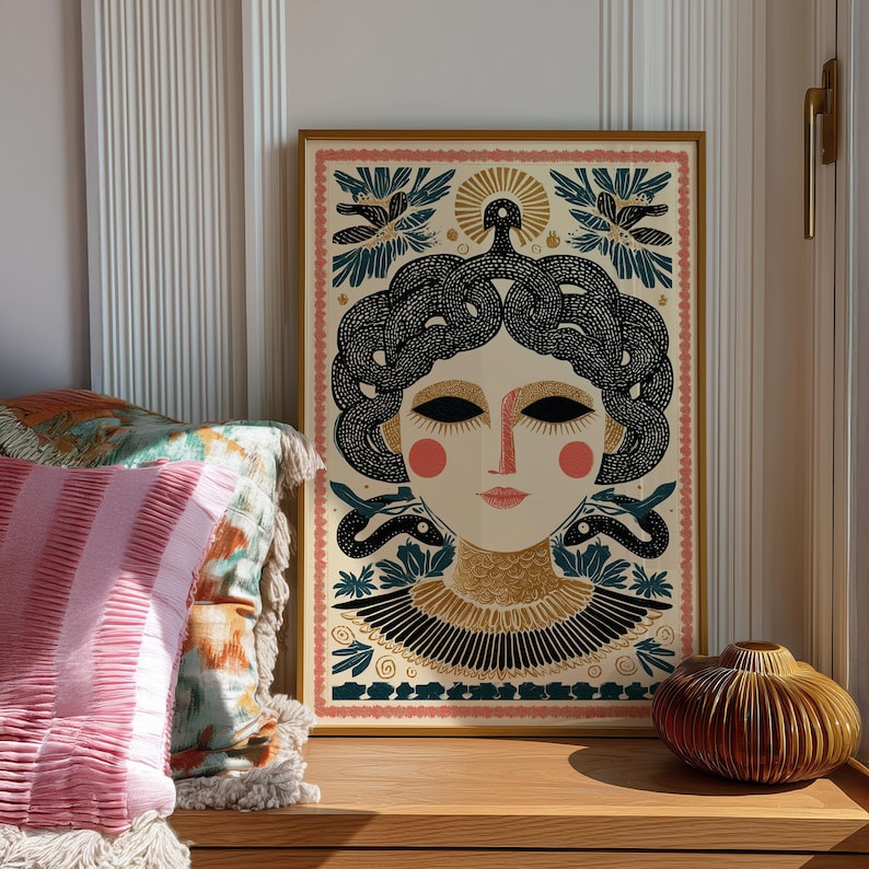 May include: A framed art print featuring a stylized illustration of a woman with snakes for hair. The artwork has a gold frame and a cream background with black, gold, and teal accents. The woman has pink cheeks and a gold collar.