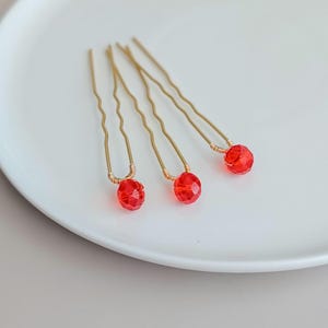 May include: Three gold hair pins with red faceted glass beads at the end.