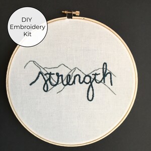 May include: DIY embroidery kit featuring the word "strength" stitched in dark teal thread with a mountain range design in gray thread.