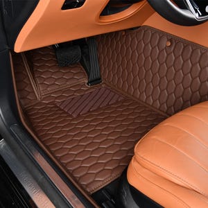 May include: Brown leather car floor mats with a honeycomb pattern. The mats are installed in a car with brown leather seats.