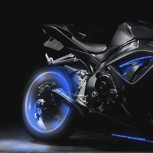 May include: A black sport motorcycle with blue LED lighting accents. The motorcycle's wheels and undercarriage are illuminated with bright blue lights, creating a striking visual effect against the dark background. The image highlights the sleek design and custom modifications.