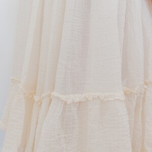 May include: A white cotton dress with a tiered skirt and a scalloped hem. The dress has a simple, classic design and is perfect for a variety of occasions.