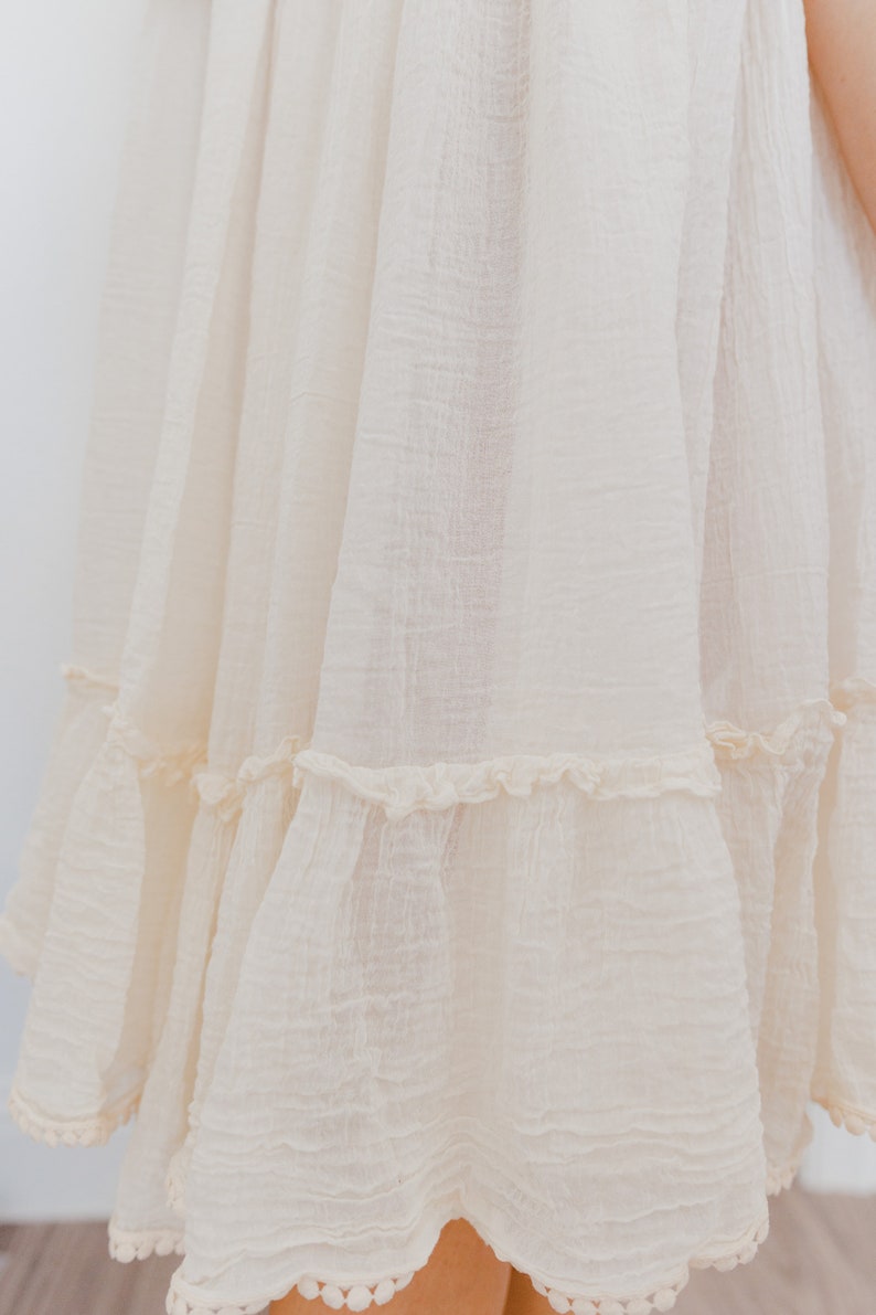 May include: A white cotton dress with a tiered skirt and a scalloped hem. The dress has a simple, classic design and is perfect for a variety of occasions.