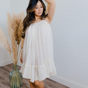 May include: A white, flowing, sleeveless dress with a ruffled hem. The dress is made from a lightweight fabric and has a relaxed fit.