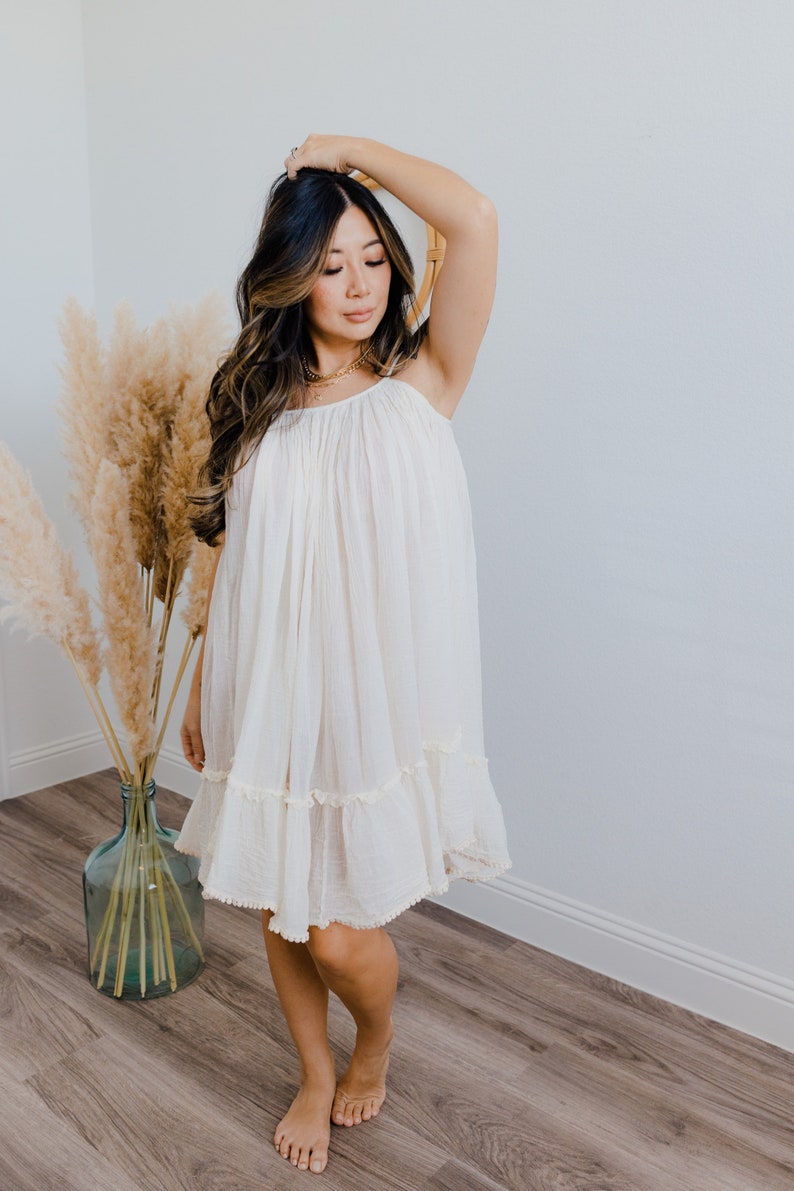 May include: A white, flowing, sleeveless dress with a ruffled hem. The dress is made from a lightweight fabric and has a relaxed fit.