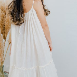 May include: A white, sleeveless, midi-length dress with a ruffled hem. The dress has a loose, flowy fit and is made of a lightweight fabric.