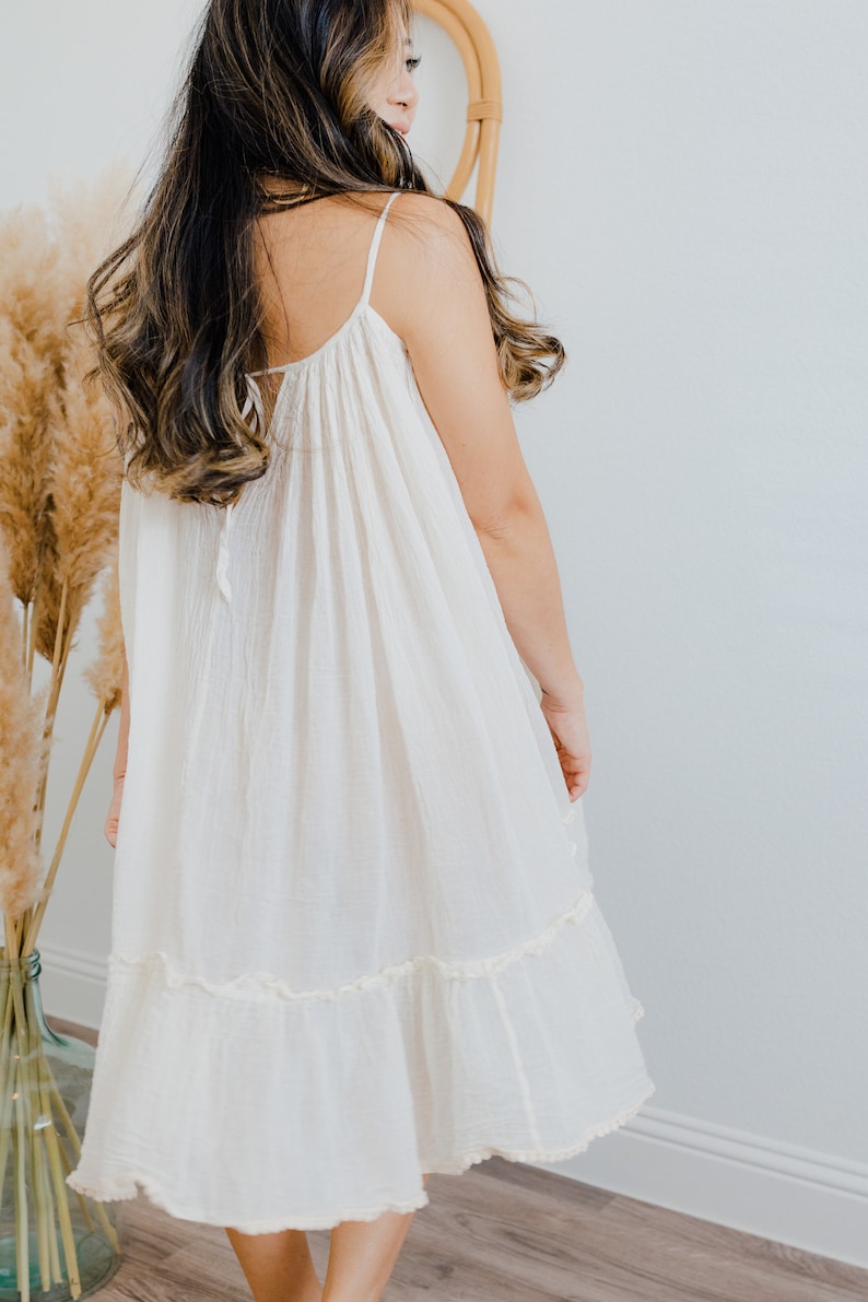 May include: A white, sleeveless, midi-length dress with a ruffled hem. The dress has a loose, flowy fit and is made of a lightweight fabric.
