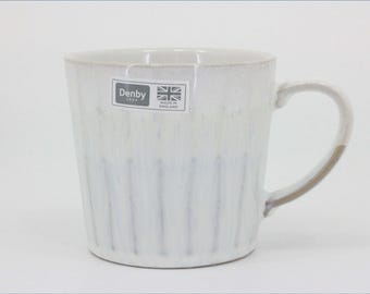 May include: A ceramic mug with a white and light gray glazed finish featuring vertical ribbed textures. A rectangular sticker on the side displays the text Denby 1809 with a Union Jack flag icon and the words Made in England. It has a curved handle.