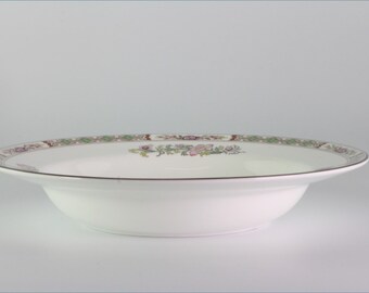 May include: A white ceramic bowl with a green, brown, and pink floral pattern around the rim. The bowl is oval shaped and has a slight lip.
