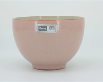 May include: A dusty pink ceramic bowl with a smooth, speckled finish and a rounded shape. A rectangular sticker on the front features the text Denby and a small Union Jack flag icon with the words Made in England printed below the flag.